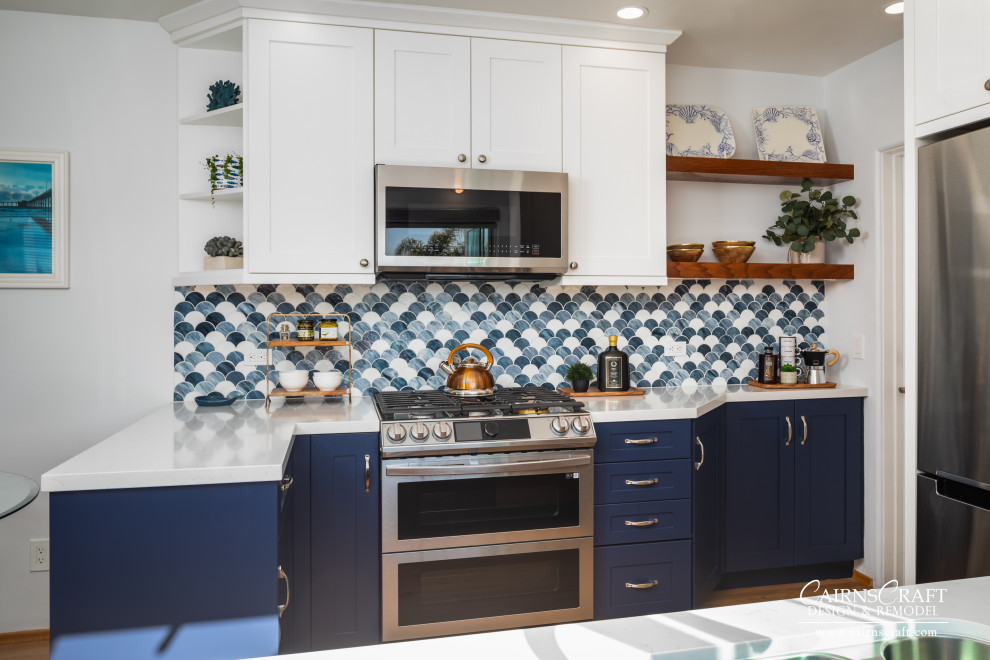 Bild på ett mellanstort maritimt vit vitt kök, med en dubbel diskho, vita skåp, bänkskiva i kvarts, blått stänkskydd, rostfria vitvaror, mellanmörkt trägolv, en halv köksö, brunt golv, skåp i shakerstil och glaspanel som stänkskydd