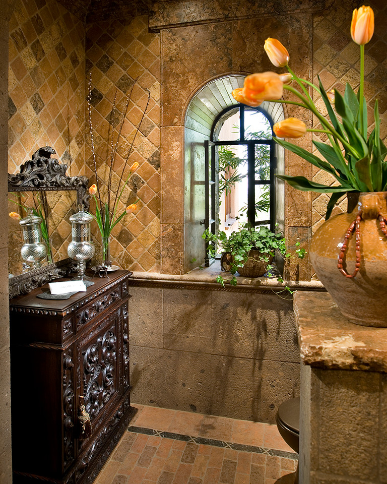 This is an example of a mid-sized mediterranean bathroom in Phoenix with furniture-like cabinets, dark wood cabinets, wood benchtops, stone tile, multi-coloured walls, brick floors and brown floor.