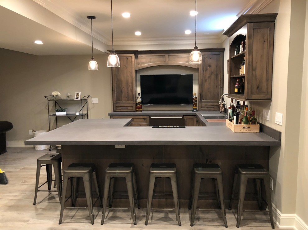Mid-sized country u-shaped seated home bar in New York with an undermount sink, recessed-panel cabinets, dark wood cabinets, solid surface benchtops, light hardwood floors, beige floor and grey benchtop.