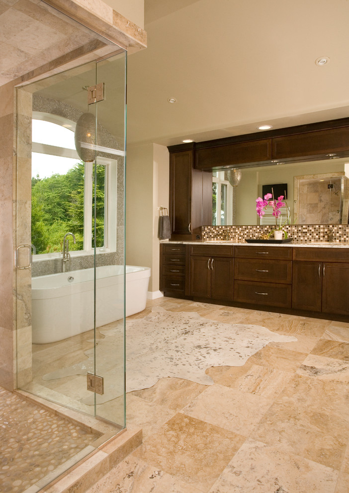 Photo of a large transitional master wet room bathroom in Seattle with shaker cabinets, dark wood cabinets, a freestanding tub, a two-piece toilet, beige tile, travertine, beige walls, travertine floors, an undermount sink, granite benchtops, beige floor, a hinged shower door and multi-coloured benchtops.