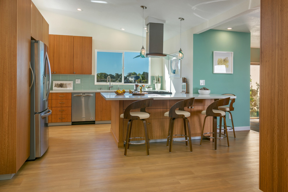 Mid-sized midcentury l-shaped open plan kitchen in San Diego with a double-bowl sink, flat-panel cabinets, light wood cabinets, quartz benchtops, green splashback, glass tile splashback, stainless steel appliances, light hardwood floors, with island, beige floor and white benchtop.