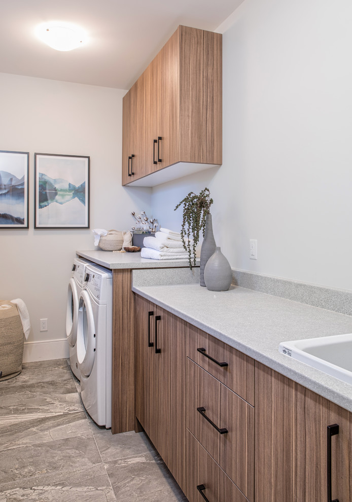 Photo of a contemporary single-wall dedicated laundry room in Other with flat-panel cabinets, light wood cabinets, a side-by-side washer and dryer and grey benchtop.