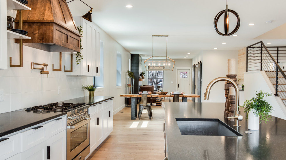 Eat-in kitchen - mid-sized cottage galley light wood floor and beige floor eat-in kitchen idea in Denver with an undermount sink, shaker cabinets, white cabinets, white backsplash, ceramic backsplash, stainless steel appliances, an island and black countertops