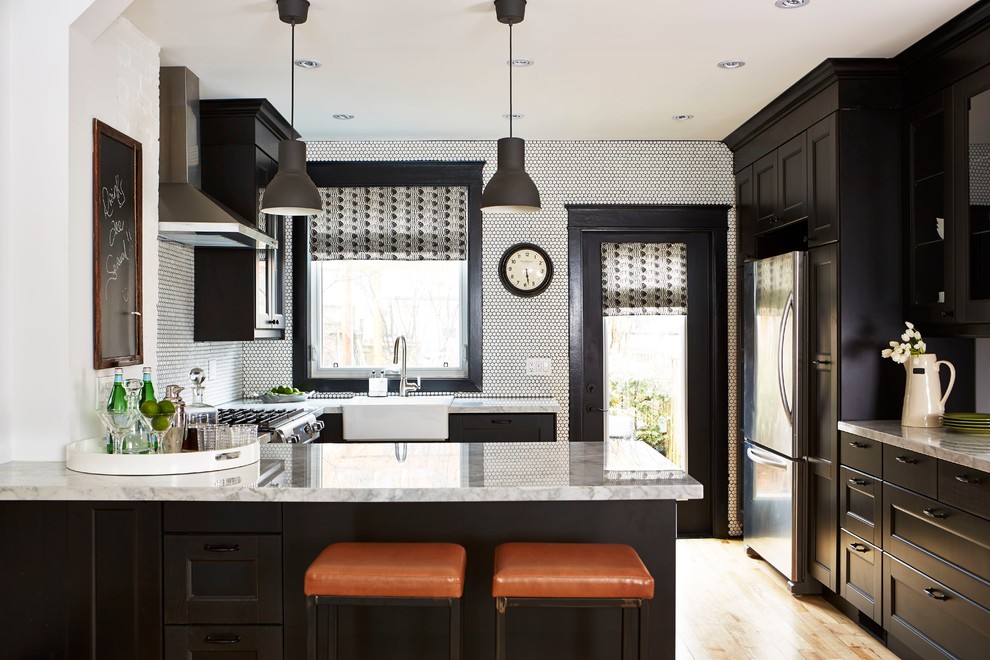 This is an example of a transitional u-shaped kitchen in Toronto with a farmhouse sink, recessed-panel cabinets, stainless steel appliances, light hardwood floors and a peninsula.