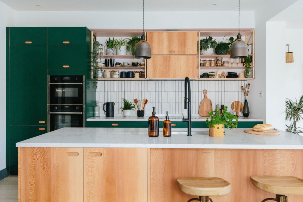 This is an example of a medium sized scandi open plan kitchen in London with an integrated sink, flat-panel cabinets, green cabinets, white splashback, ceramic splashback, coloured appliances, laminate floors, an island and grey floors.