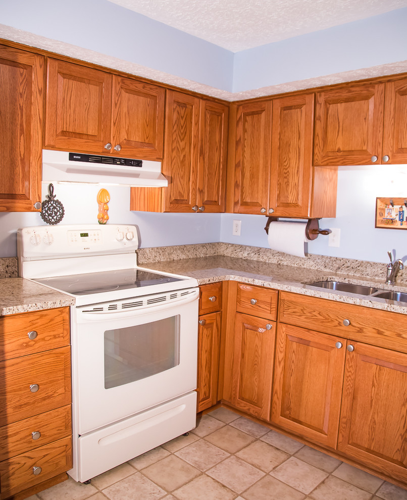 Kitchen - small rustic l-shaped kitchen idea in Baltimore with a double-bowl sink, raised-panel cabinets, medium tone wood cabinets, blue backsplash, white appliances and no island