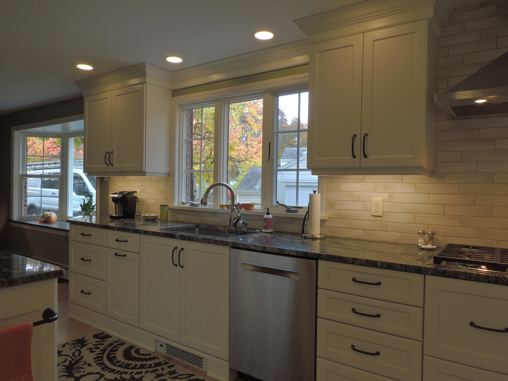 Inspiration for a transitional light wood floor eat-in kitchen remodel with a single-bowl sink, shaker cabinets, white cabinets, granite countertops, white backsplash, ceramic backsplash, stainless steel appliances, an island and black countertops