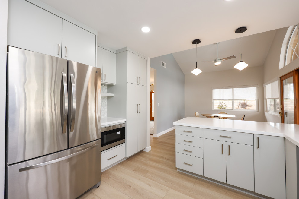 Example of a mid-sized transitional l-shaped vinyl floor and brown floor eat-in kitchen design in San Diego with a triple-bowl sink, flat-panel cabinets, gray cabinets, quartz countertops, white backsplash, glass tile backsplash, stainless steel appliances, a peninsula and white countertops