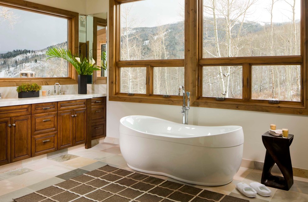 Photo of a country bathroom in Denver with raised-panel cabinets, dark wood cabinets, a freestanding tub, white walls and an undermount sink.
