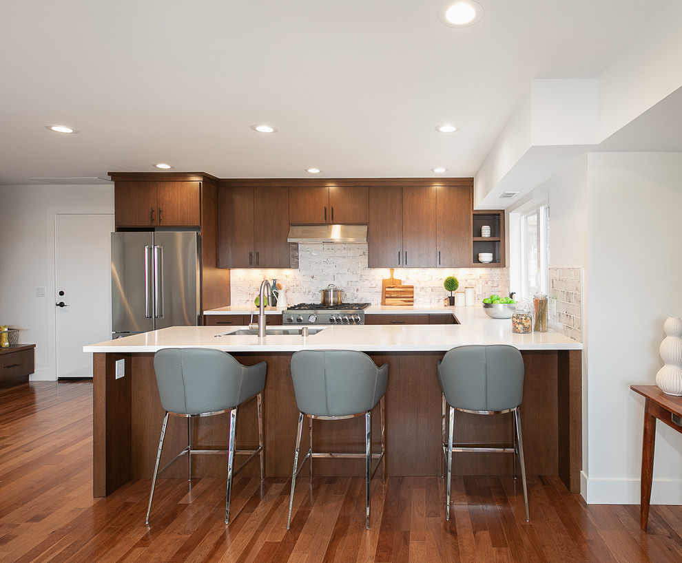 Photo of a contemporary u-shaped kitchen in Seattle with an undermount sink, flat-panel cabinets, dark wood cabinets, white splashback, stainless steel appliances, dark hardwood floors, a peninsula and white benchtop.