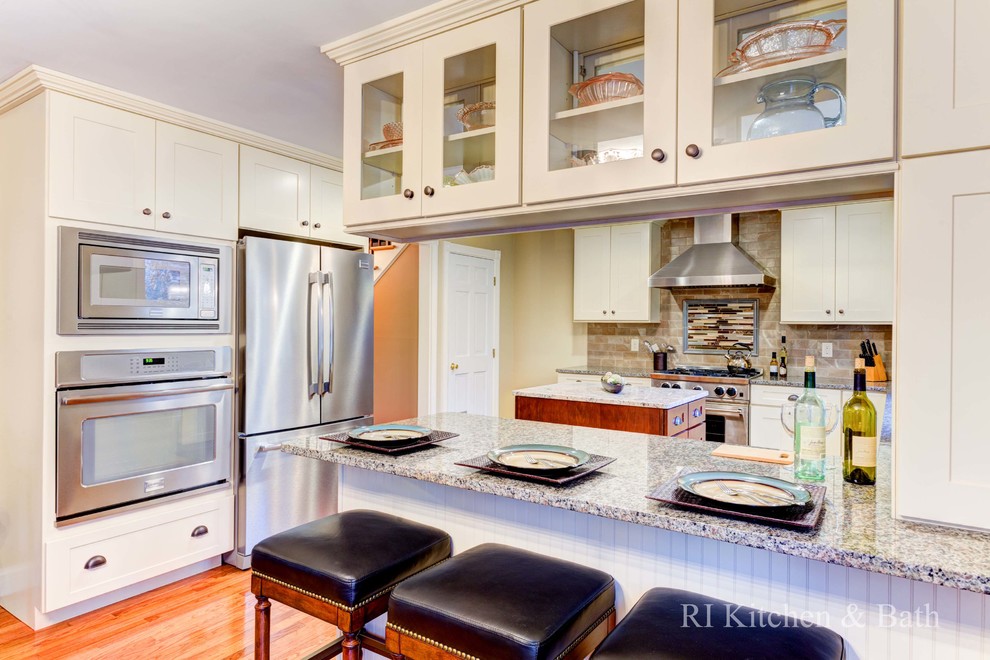 Example of a large transitional u-shaped light wood floor eat-in kitchen design in Providence with an undermount sink, shaker cabinets, beige cabinets, granite countertops, brown backsplash, porcelain backsplash, stainless steel appliances and an island