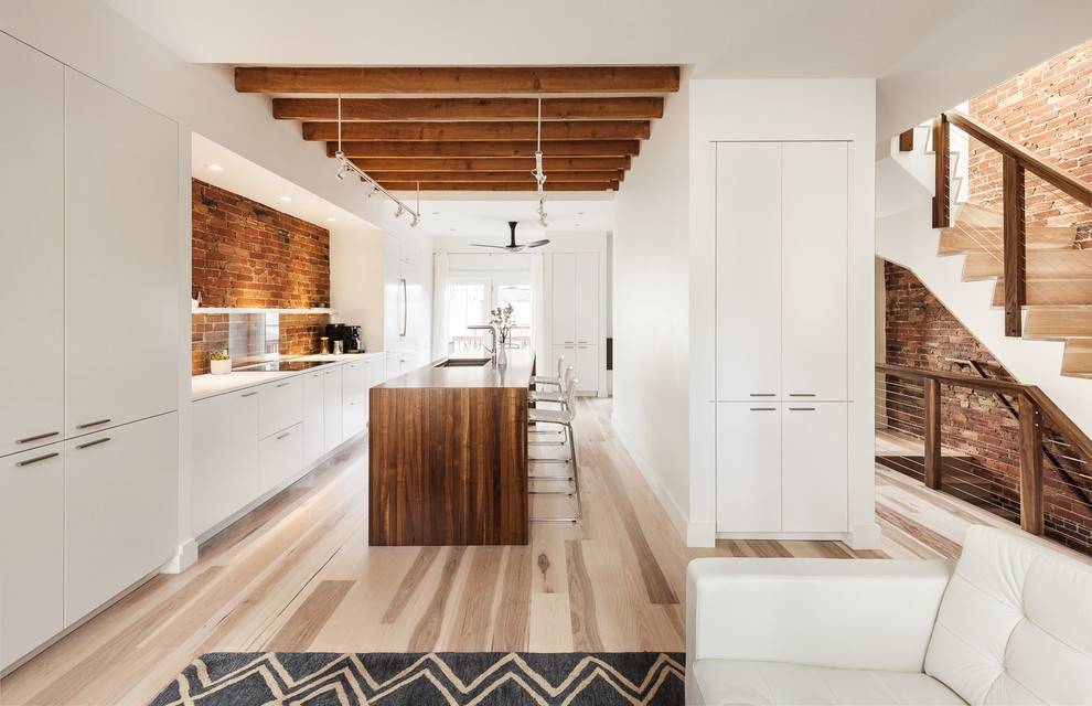 This is an example of a large contemporary single-wall eat-in kitchen in Boston with an undermount sink, flat-panel cabinets, white cabinets, wood benchtops, red splashback, glass sheet splashback, white appliances, light hardwood floors and with island.