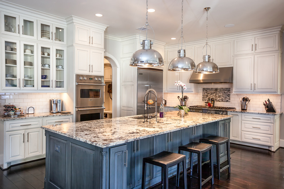 Design ideas for a mid-sized traditional l-shaped open plan kitchen in Houston with a drop-in sink, raised-panel cabinets, white cabinets, granite benchtops, white splashback, subway tile splashback, stainless steel appliances, dark hardwood floors and with island.