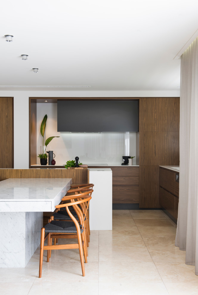 Mid-sized modern l-shaped open plan kitchen in Sydney with a double-bowl sink, flat-panel cabinets, medium wood cabinets, solid surface benchtops, white splashback, glass sheet splashback, stainless steel appliances, limestone floors, with island and beige floor.