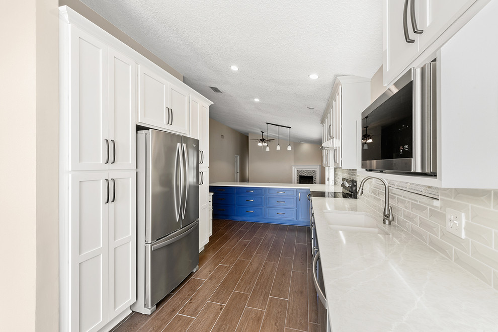 Inspiration for a large transitional l-shaped vinyl floor and brown floor open concept kitchen remodel in Jacksonville with an undermount sink, shaker cabinets, blue cabinets, quartzite countertops, white backsplash, ceramic backsplash, stainless steel appliances and a peninsula
