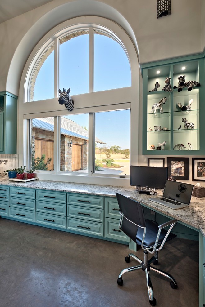 This is an example of a large transitional home office in Austin with blue walls, concrete floors and a built-in desk.