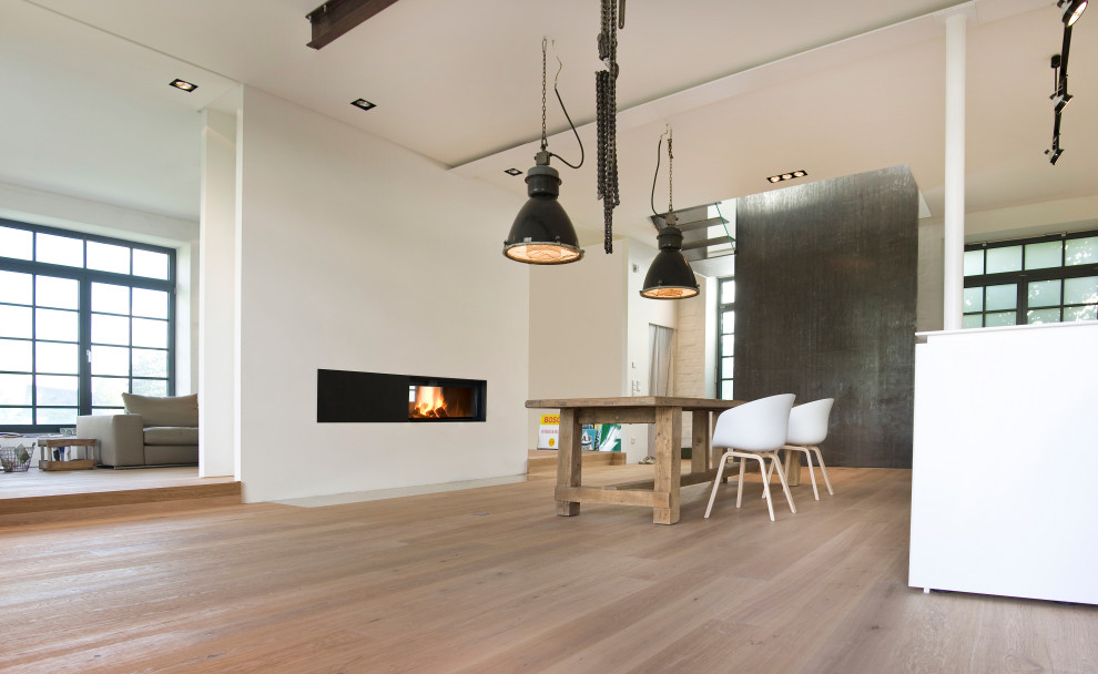 This is an example of a large contemporary formal loft-style living room in Munich with white walls, medium hardwood floors, a wood stove, a plaster fireplace surround, no tv and beige floor.