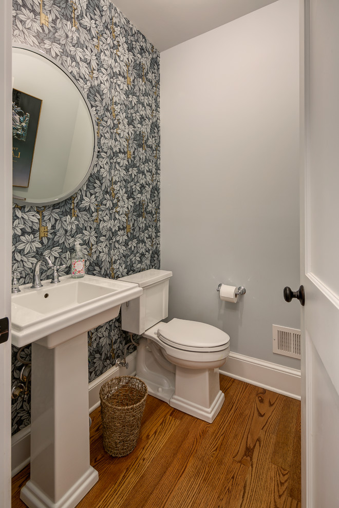 Photo of a small traditional powder room in Orange County with a two-piece toilet, medium hardwood floors, a pedestal sink, multi-coloured walls and brown floor.
