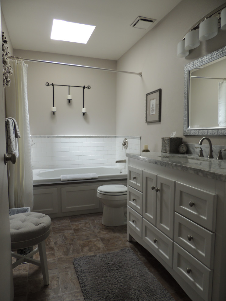 Exempel på ett grå grått badrum, med vita skåp, ett platsbyggt badkar, en toalettstol med hel cisternkåpa, vit kakel, porslinskakel, grå väggar, laminatgolv, ett undermonterad handfat, marmorbänkskiva och brunt golv