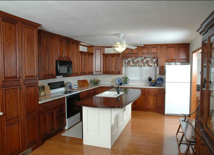 Kitchen - mid-sized l-shaped light wood floor kitchen idea with medium tone wood cabinets, white backsplash, white appliances and an island