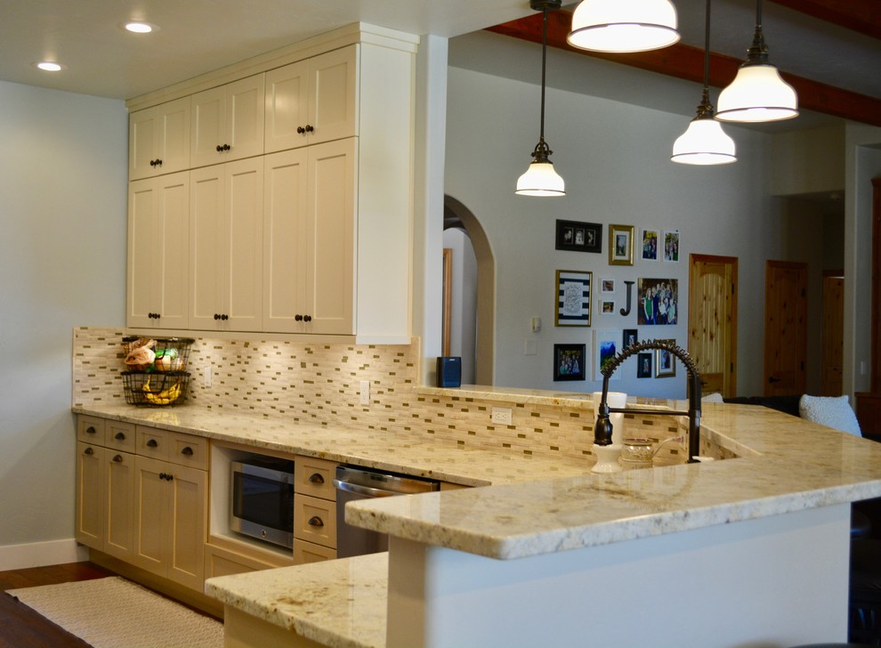 Mid-sized traditional u-shaped eat-in kitchen in Albuquerque with an undermount sink, shaker cabinets, white cabinets, granite benchtops, beige splashback, mosaic tile splashback, stainless steel appliances, medium hardwood floors, brown floor and a peninsula.