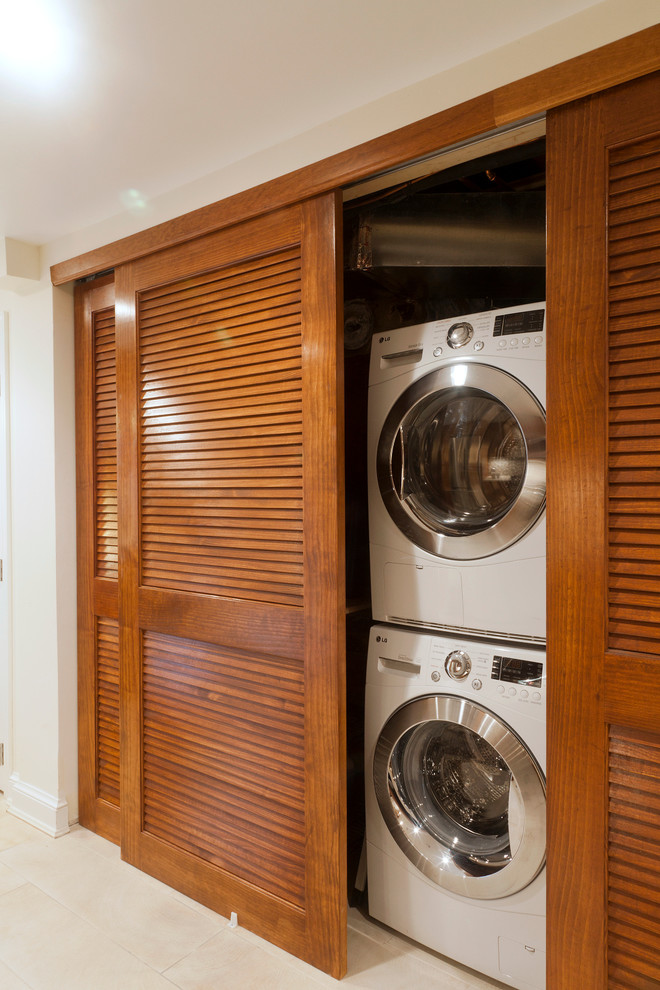 Photo of a mid-sized contemporary l-shaped laundry cupboard in DC Metro with an undermount sink, shaker cabinets, medium wood cabinets, ceramic floors, beige walls and a stacked washer and dryer.