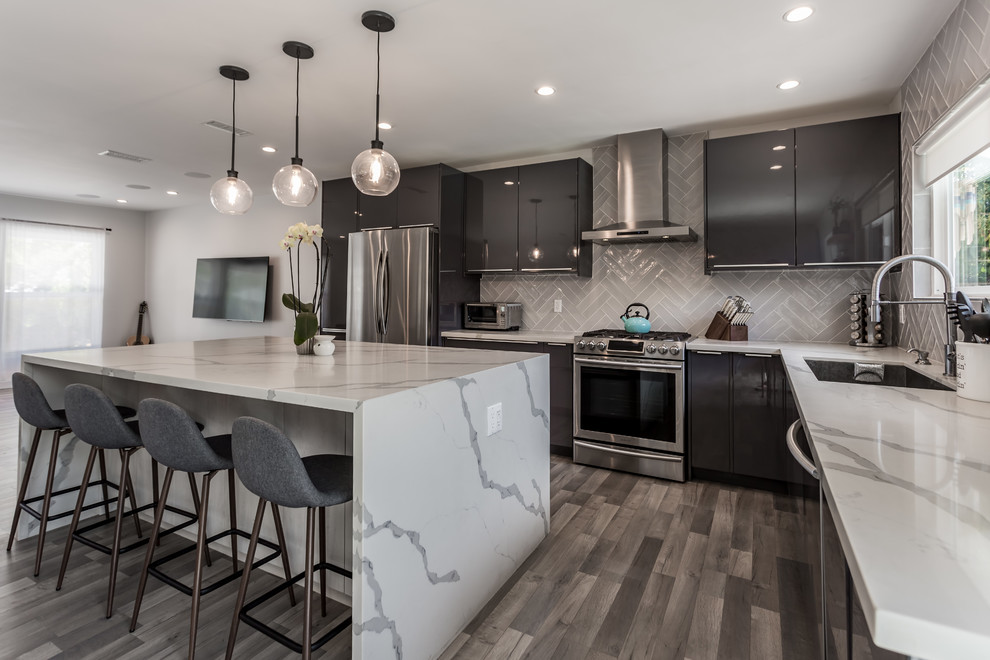 Expansive contemporary l-shaped open plan kitchen in Los Angeles with an undermount sink, flat-panel cabinets, black cabinets, marble benchtops, white splashback, subway tile splashback, stainless steel appliances, vinyl floors, with island, multi-coloured floor and white benchtop.