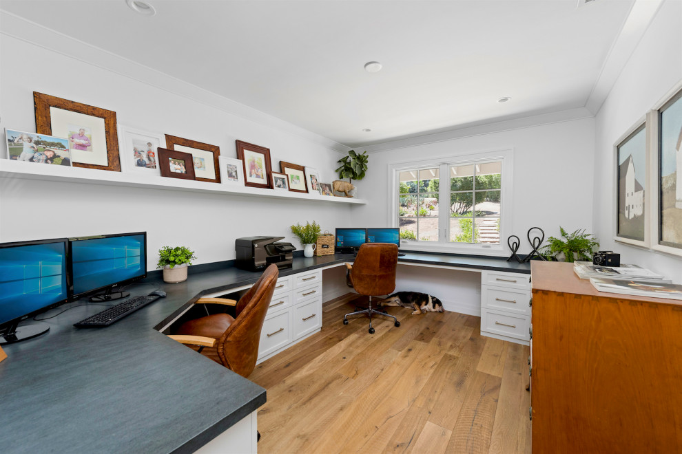 This is an example of a transitional home office in San Diego with white walls, medium hardwood floors, a built-in desk and brown floor.