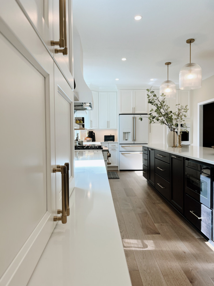 Eat-in kitchen - large transitional l-shaped light wood floor and beige floor eat-in kitchen idea with a farmhouse sink, shaker cabinets, white cabinets, quartz countertops, white backsplash, ceramic backsplash, white appliances, an island and white countertops