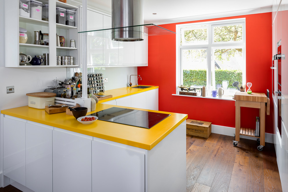 Inspiration for a mid-sized eclectic l-shaped kitchen in London with a drop-in sink, flat-panel cabinets, white cabinets, solid surface benchtops, white splashback, glass sheet splashback, panelled appliances, dark hardwood floors, brown floor, yellow benchtop and a peninsula.