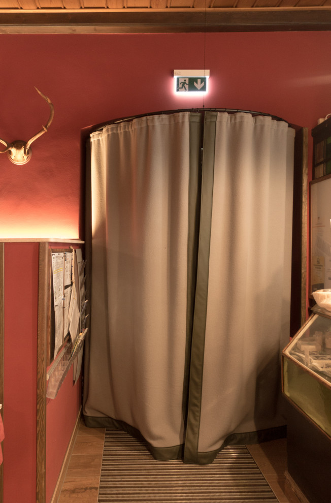 Imagen de salón abierto rústico de tamaño medio con paredes rojas, suelo de baldosas de porcelana, estufa de leña, marco de chimenea de baldosas y/o azulejos, suelo marrón, vigas vistas y boiserie