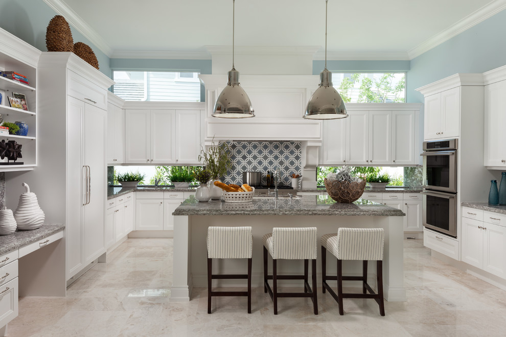 Inspiration for a beach style u-shaped kitchen in Miami with an undermount sink, recessed-panel cabinets, white cabinets, window splashback, stainless steel appliances, with island, beige floor and grey benchtop.