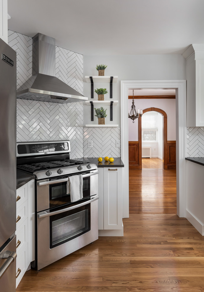 Mid-sized transitional u-shaped light wood floor and brown floor enclosed kitchen photo in Boston with an undermount sink, shaker cabinets, white cabinets, quartz countertops, gray backsplash, ceramic backsplash, stainless steel appliances, a peninsula and gray countertops