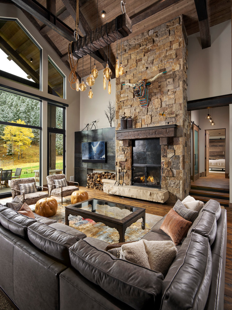 Large country open concept living room in Denver with white walls, a standard fireplace, a stone fireplace surround, a wall-mounted tv, brown floor and dark hardwood floors.