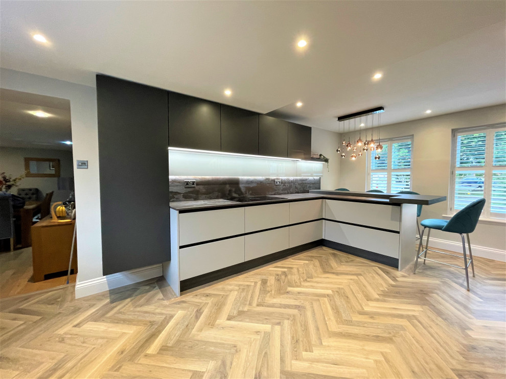 Cette image montre une cuisine américaine design en L et bois foncé de taille moyenne avec un évier 1 bac, un placard à porte plane, un plan de travail en quartz modifié, un électroménager noir et un sol en vinyl.