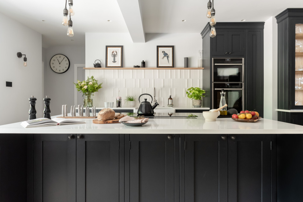 Design ideas for a large traditional u-shaped eat-in kitchen in Surrey with a farmhouse sink, shaker cabinets, black cabinets, quartzite benchtops, white splashback, ceramic splashback, black appliances, ceramic floors, with island and white benchtop.