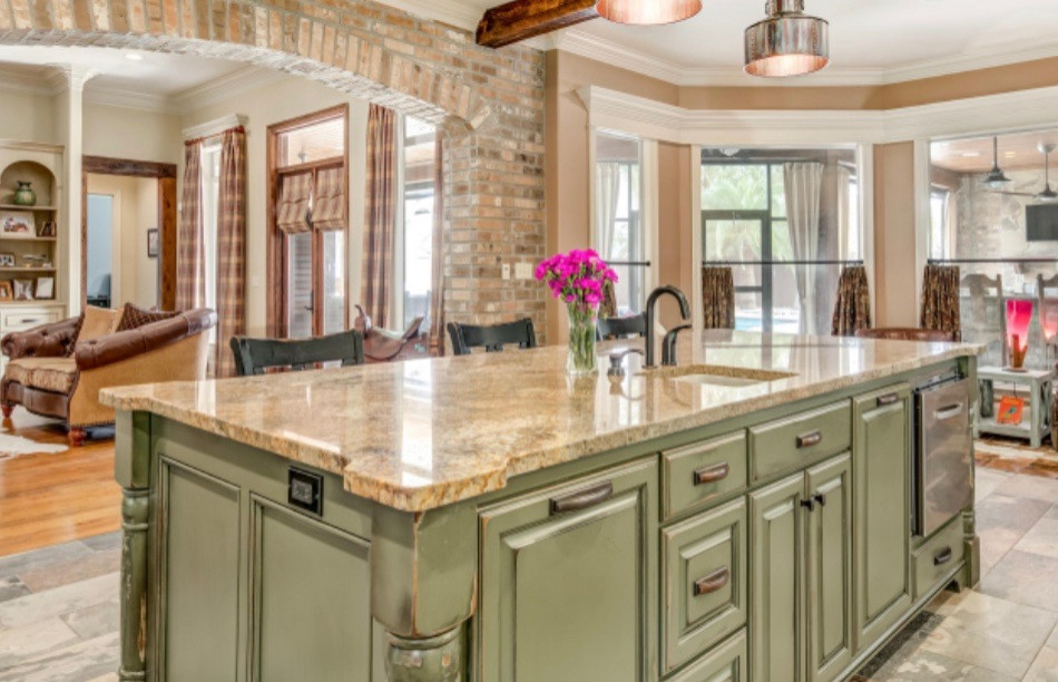 Photo of a mid-sized country l-shaped eat-in kitchen in Houston with a farmhouse sink, raised-panel cabinets, distressed cabinets, granite benchtops, multi-coloured splashback, glass tile splashback, stainless steel appliances, ceramic floors, with island, grey floor, beige benchtop and recessed.