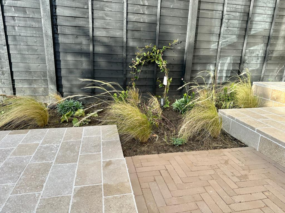 Photo of a small contemporary partial sun garden for autumn in London with a garden path, natural stone paving and a wood fence.
