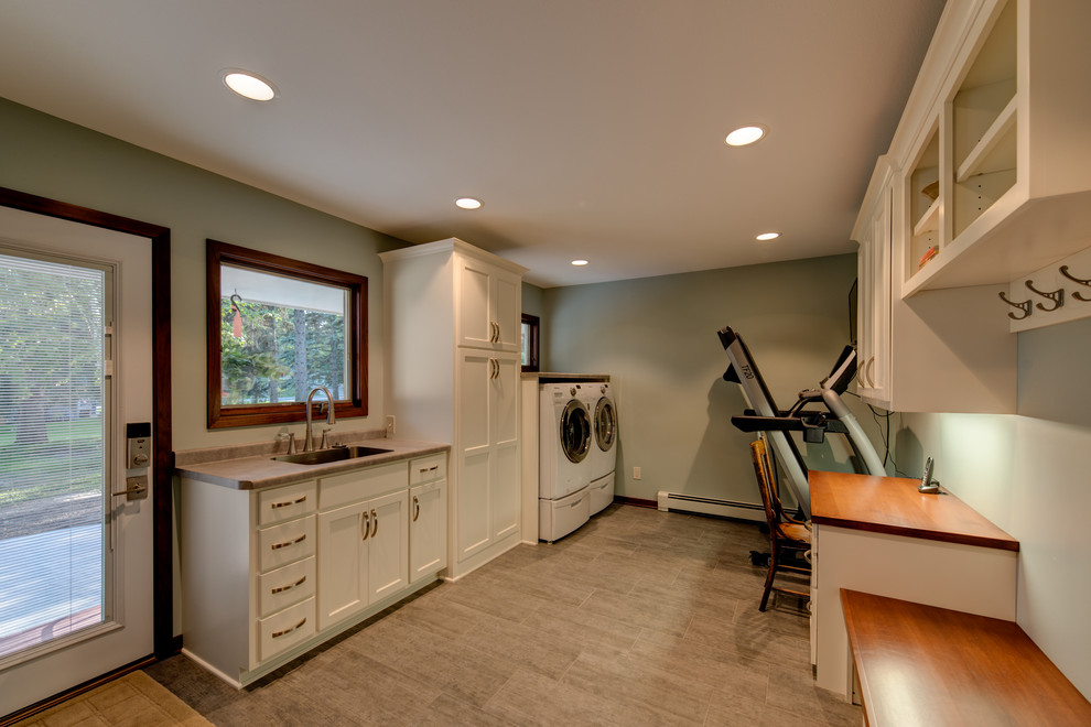 Inspiration for a large transitional single-wall utility room in Minneapolis with an integrated sink, raised-panel cabinets, white cabinets, laminate benchtops, porcelain floors, a side-by-side washer and dryer, beige floor and grey walls.