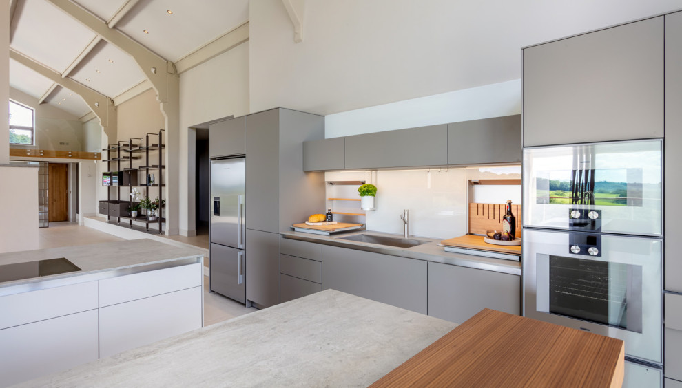 Inspiration for an expansive modern u-shaped open plan kitchen in Other with an integrated sink, flat-panel cabinets, grey cabinets, solid surface benchtops, white splashback, glass sheet splashback, stainless steel appliances, ceramic floors, multiple islands and grey benchtop.