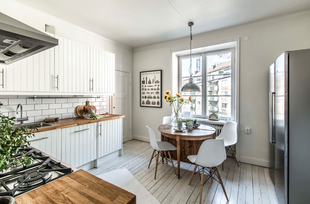 This is an example of a country kitchen in Stockholm with wood benchtops, subway tile splashback, light hardwood floors, no island, beige floor and brown benchtop.