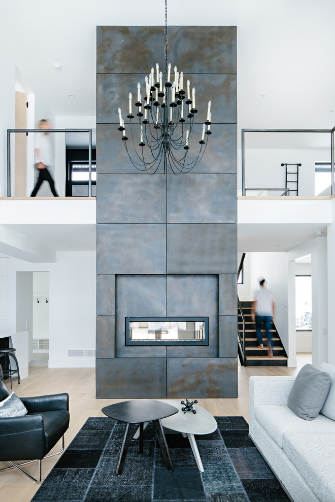 This is an example of a contemporary open concept living room in Other with white walls, light hardwood floors, a standard fireplace, a concrete fireplace surround and white floor.
