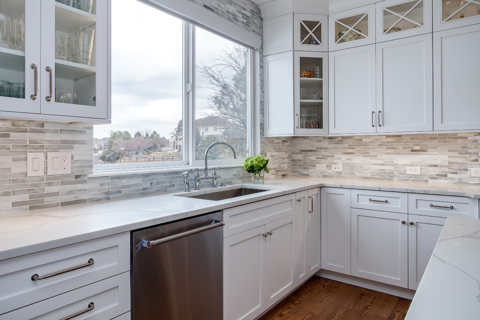 Mid-sized transitional u-shaped eat-in kitchen in Denver with an undermount sink, shaker cabinets, white cabinets, quartzite benchtops, multi-coloured splashback, stainless steel appliances, medium hardwood floors, with island, matchstick tile splashback, brown floor and white benchtop.