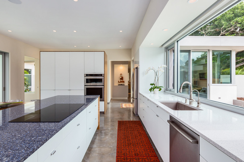 This is an example of a mid-sized modern l-shaped open plan kitchen in Other with an undermount sink, flat-panel cabinets, white cabinets, quartz benchtops, glass sheet splashback, stainless steel appliances, concrete floors, with island, grey floor and blue benchtop.