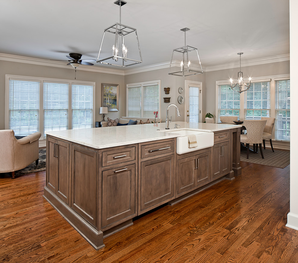 Photo of a large traditional eat-in kitchen in Charlotte with a farmhouse sink, recessed-panel cabinets, white cabinets, quartz benchtops, beige splashback, ceramic splashback, stainless steel appliances, medium hardwood floors, with island, brown floor and white benchtop.