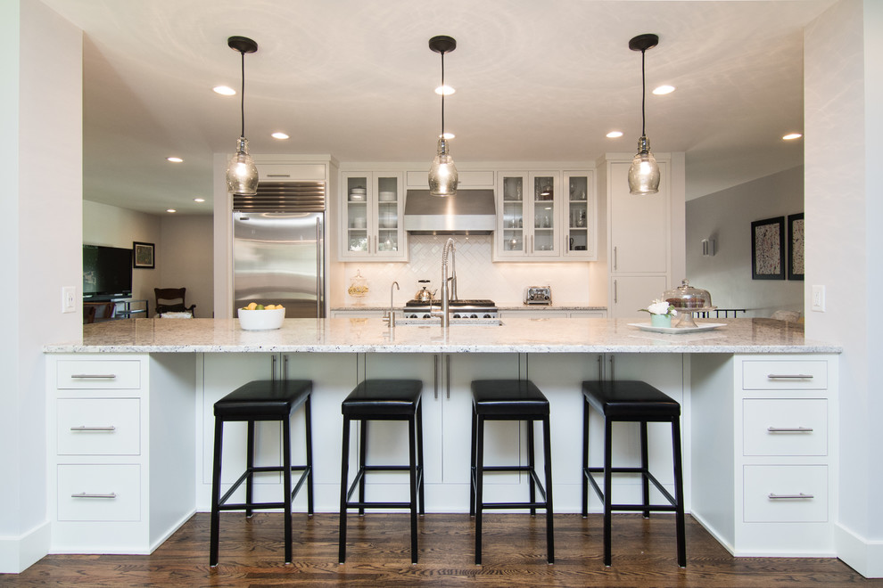 This is an example of a transitional galley kitchen in Minneapolis with glass-front cabinets, white cabinets, white splashback, stainless steel appliances, dark hardwood floors and a peninsula.