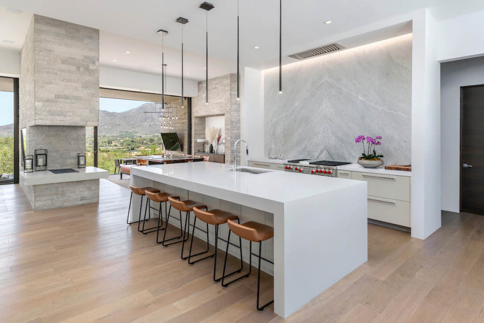 Contemporary open plan kitchen in Phoenix with an undermount sink, flat-panel cabinets, beige cabinets, grey splashback, stainless steel appliances, light hardwood floors, with island and white benchtop.