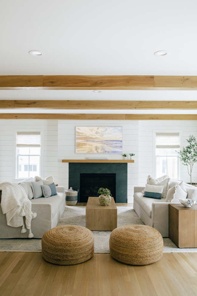 This is an example of a large beach style open concept living room in Other with white walls, light hardwood floors, a standard fireplace, a concrete fireplace surround, a wall-mounted tv, brown floor, exposed beam and planked wall panelling.