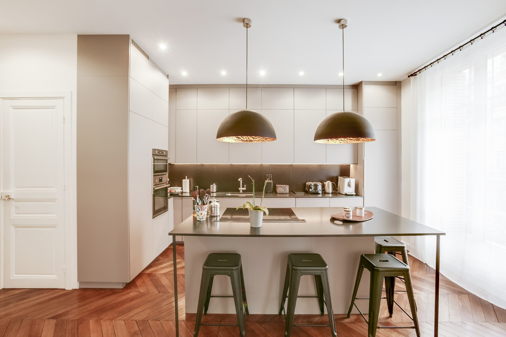 This is an example of a large modern l-shaped eat-in kitchen in Paris with an undermount sink, beaded inset cabinets, beige cabinets, granite benchtops, black splashback, marble splashback, stainless steel appliances, medium hardwood floors, with island and brown floor.