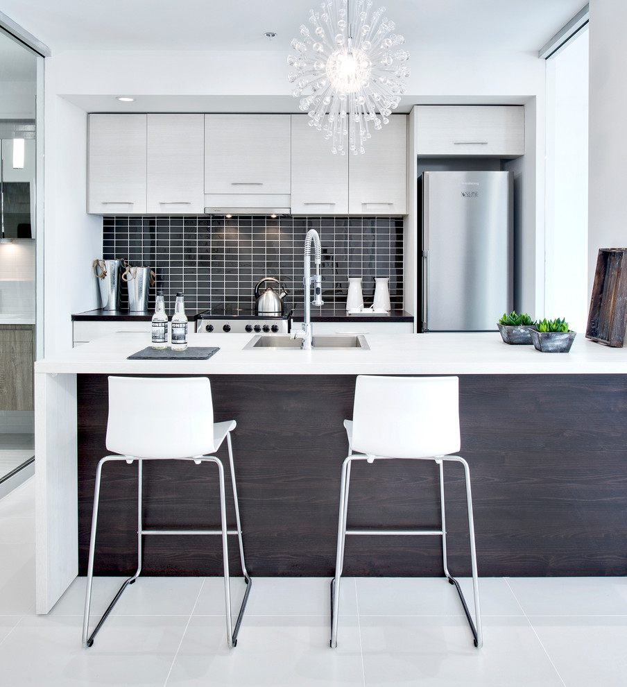 Contemporary galley separate kitchen in Montreal with a drop-in sink, flat-panel cabinets, black splashback and stainless steel appliances.